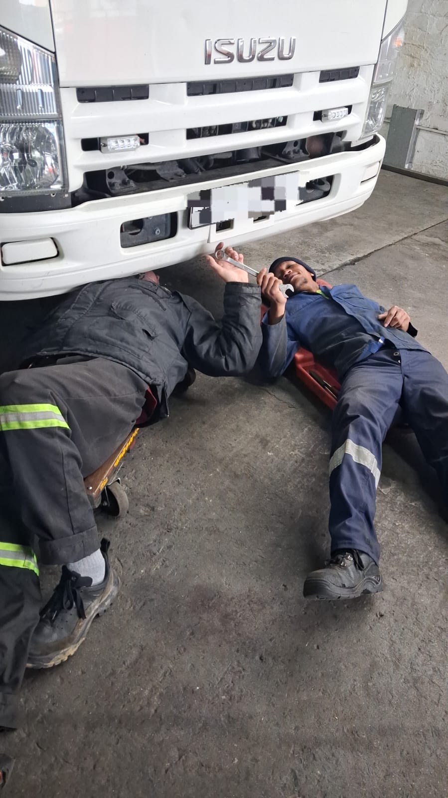 Two DTL mechanics working under an Isuzu truck