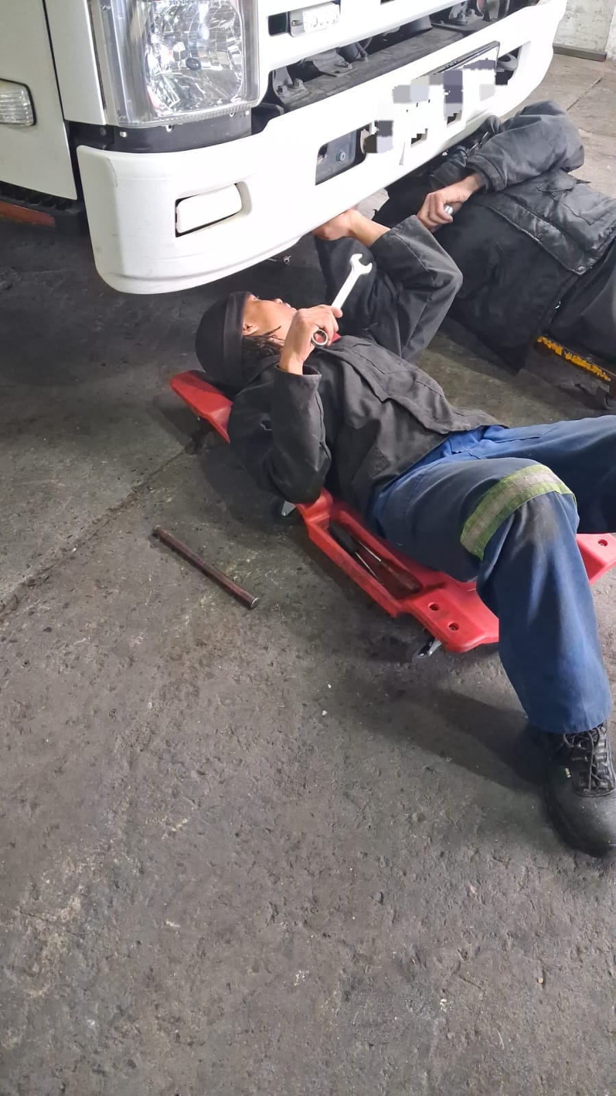 DTL mechanics loosening a bolt under an Isuzu truck